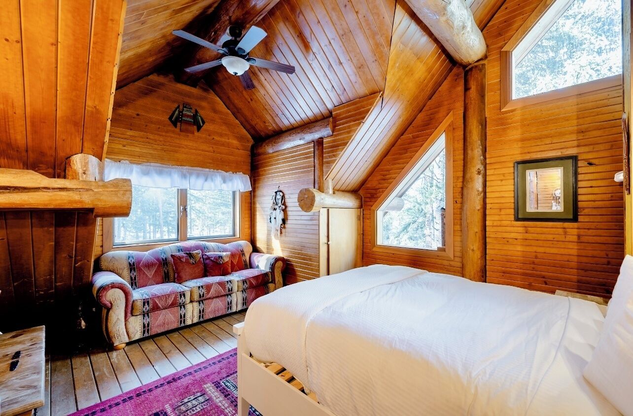 Una habitación de cabaña acogedora, con techo de madera, cama, sofá y ventana.