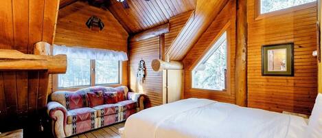 Una habitación de cabaña acogedora, con techo de madera, cama, sofá y ventana.