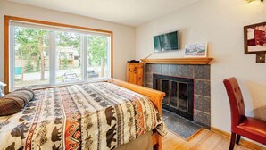 A bedroom with a large window, a fireplace, a bed with a patterned bedspread, and a TV mounted on the wall. - Four O'clock Lodge B05 (Breckenridge)