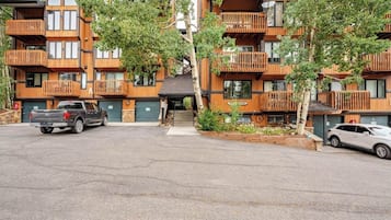 Un immeuble à plusieurs étages doté de balcons en bois, d’un espace de stationnement et d’un petit jardin.
