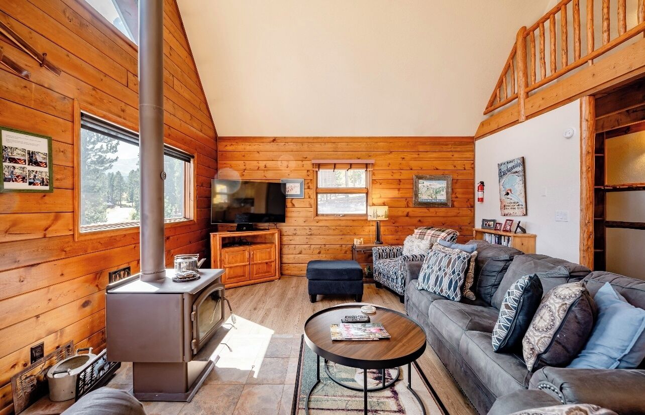 A cozy cabin interior with a wood stove, a sofa, a coffee table, and a television.