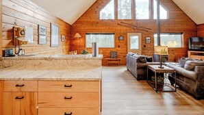 A cozy cabin interior with a kitchen area, a living room with a sofa and a television, and large windows providing natural light. - Haus Crisler (Breckenridge)