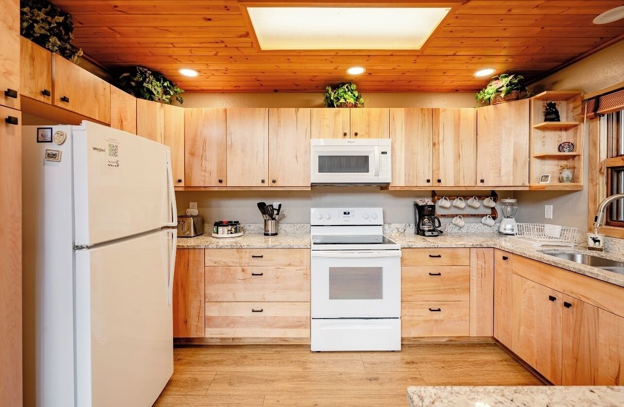 Una cocina con armarios de madera, un refrigerador, un microondas, un horno y una cafetera.