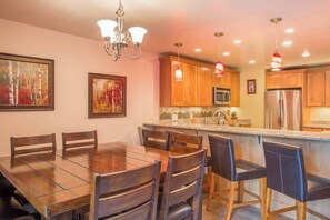 A modern kitchen with wooden cabinets, a stainless steel refrigerator, a microwave, and a dining area with a wooden table and chairs.