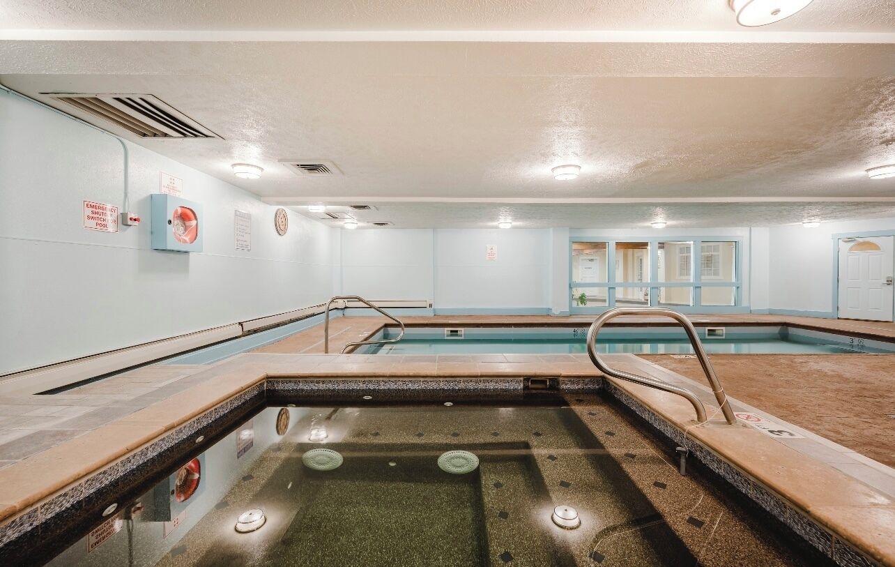 Ein Schwimmbecken mit gefliestem Deck, Sprungbrett und Rettungsschwimmerstuhl.