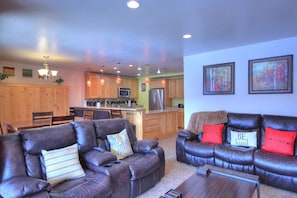 A spacious living room with leather sofas, a dining area, and a kitchen in the background.