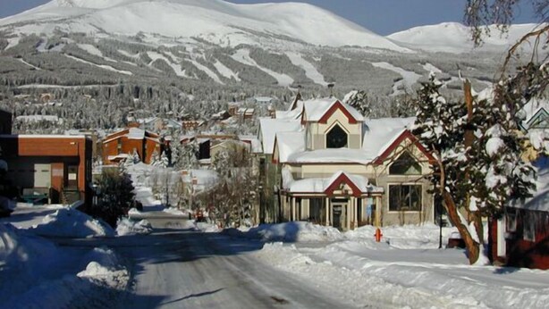 Une rue enneigée, avec des bâtiments et une montagne en arrière-plan.