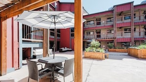 Une terrasse extérieure avec une table ronde et des chaises, un parasol et des jardinières en bois.