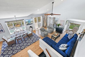 A spacious living area with a high ceiling, large windows, and a ceiling fan.