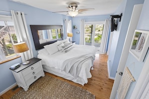 A bedroom with a bed, bedside table, lamp, and a view of greenery through the window.