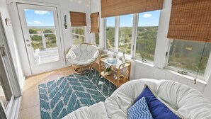 Une pièce chaleureuse avec un canapé blanc, un fauteuil en osier et une table à manger donnant sur la plage.