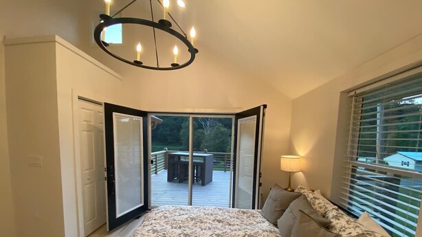 Ein Schlafzimmer mit einem großen Bett, einer Kristallleuchter, Blick auf eine Terrasse und einem Fenster mit Jalousien.