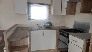 A compact kitchen with a sink, stove, and cabinets. - 8 Berth Caravan with Spacious enclosed garden (Brean)
