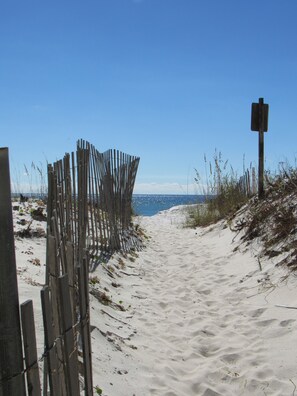 Un sentier de plage sablonneux, bordé de clôtures en bois et agrémenté d’un panneau indicateur.