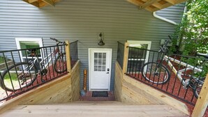 Una escalera de madera que conduce a una puerta con un cartel que dice 'Welcome', rodeada de barandillas de metal y bicicletas.