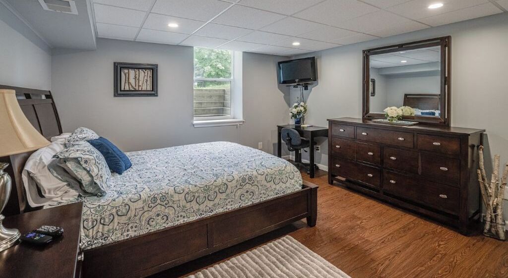 Un dormitorio con cama, cómoda, televisor y ventana.