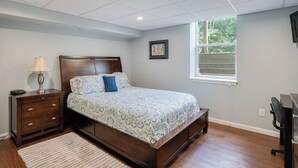 Un dormitorio con cama, mesita de noche, lámpara, cómoda y ventana con vista a zonas verdes.