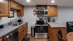 Una cocina compacta con armarios de madera, electrodomésticos de acero inoxidable, un microondas, un tostador y un cubo de basura.