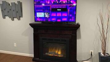 Un téléviseur à écran plat est posé sur une cheminée en bois, au-dessus d’un foyer où l’on voit des flammes.