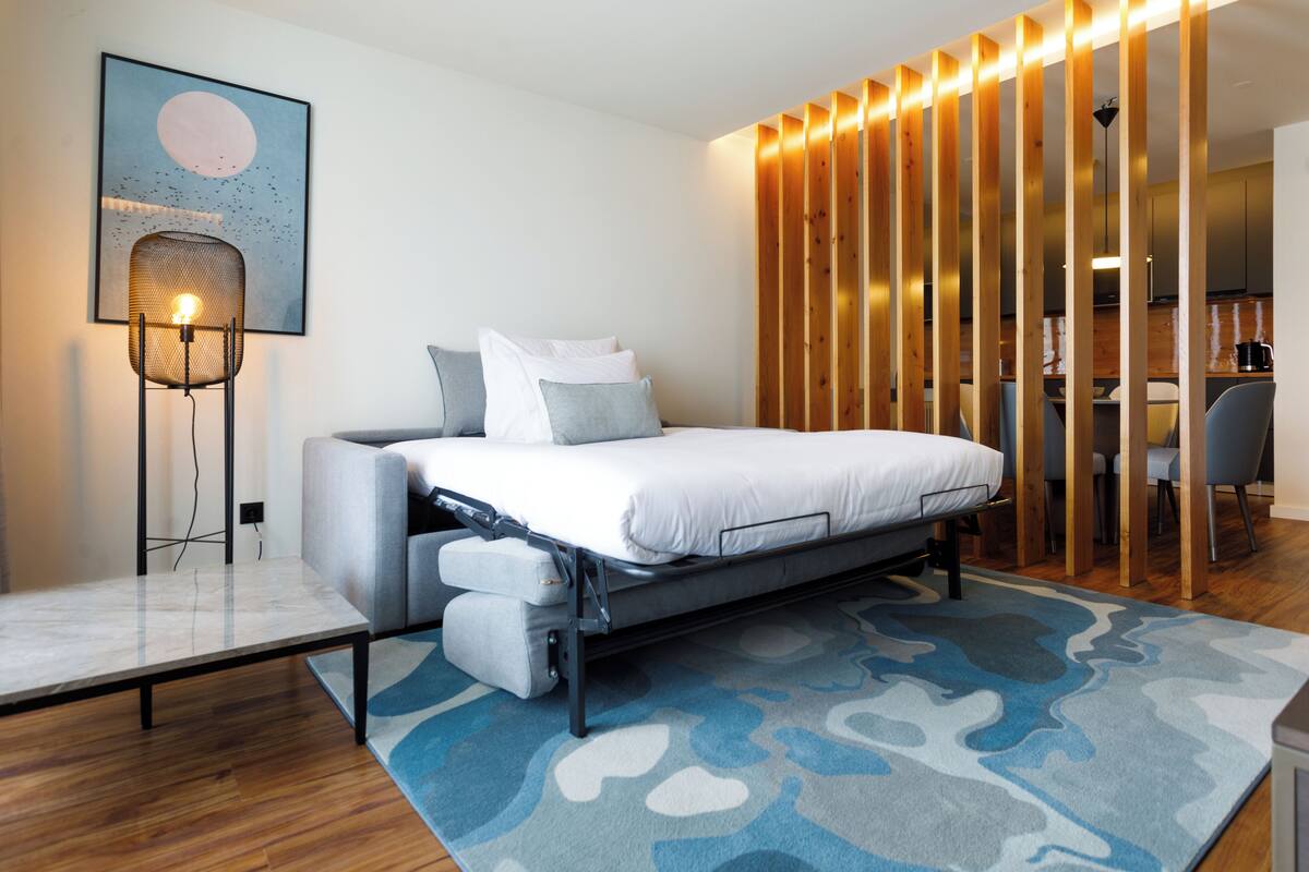 A modern bedroom with a bed, a nightstand, a wall-mounted lamp, and a wooden partition.
