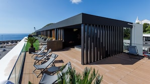 A modern outdoor deck with lounge chairs and a view of the ocean. - The Shipyard Angra (Angra do Heroismo)