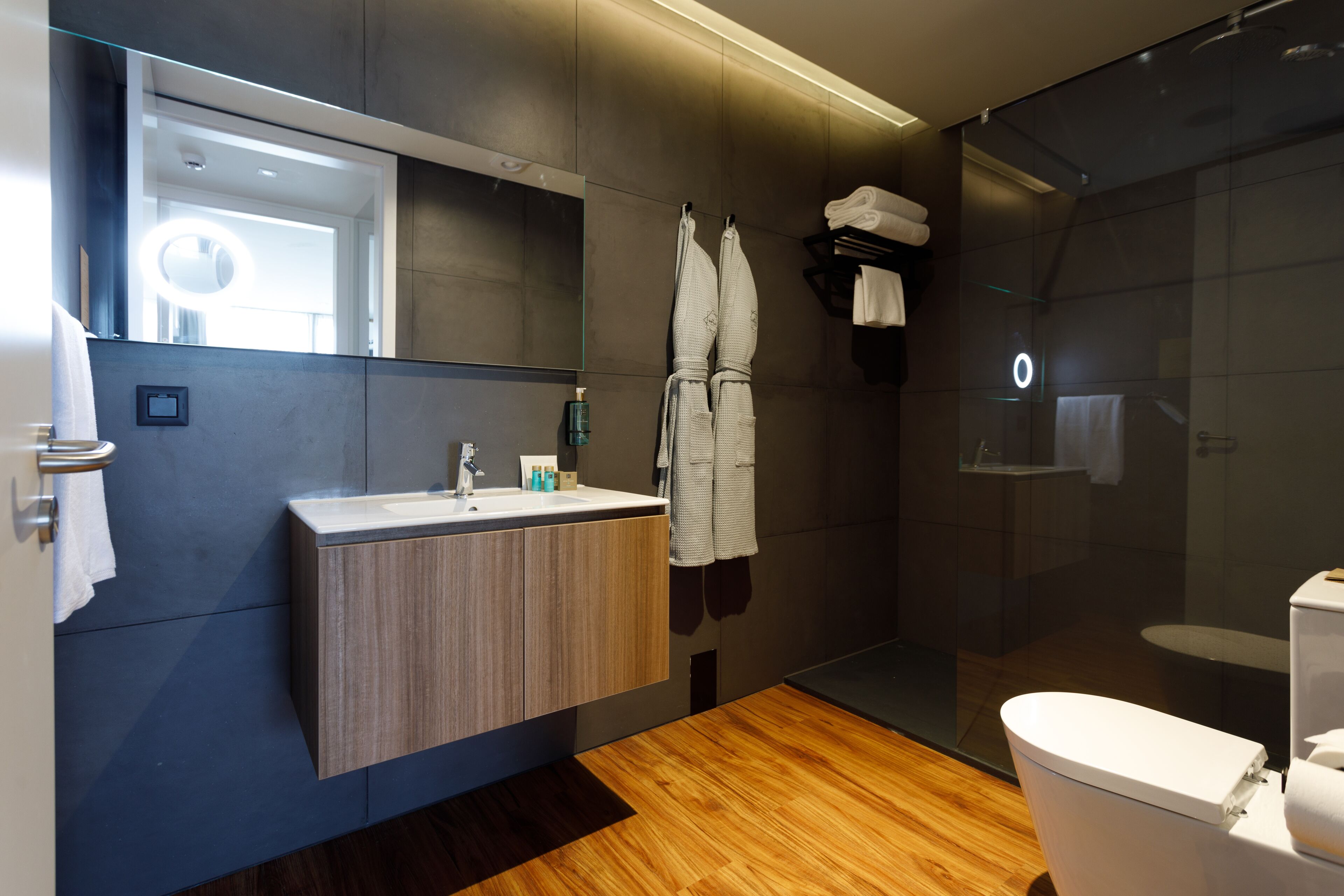 A modern bathroom with a wooden vanity, a large mirror, a glass shower enclosure, and a toilet.