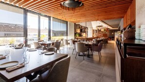 A modern restaurant with wooden ceiling beams, large windows, and a mix of dining tables and chairs. - The Shipyard Angra (Angra do Heroismo)
