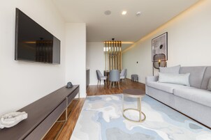 Una sala de estar moderna con un televisor de pantalla plana, un sofá gris, una mesa de centro y un comedor con sillas y una mesa.