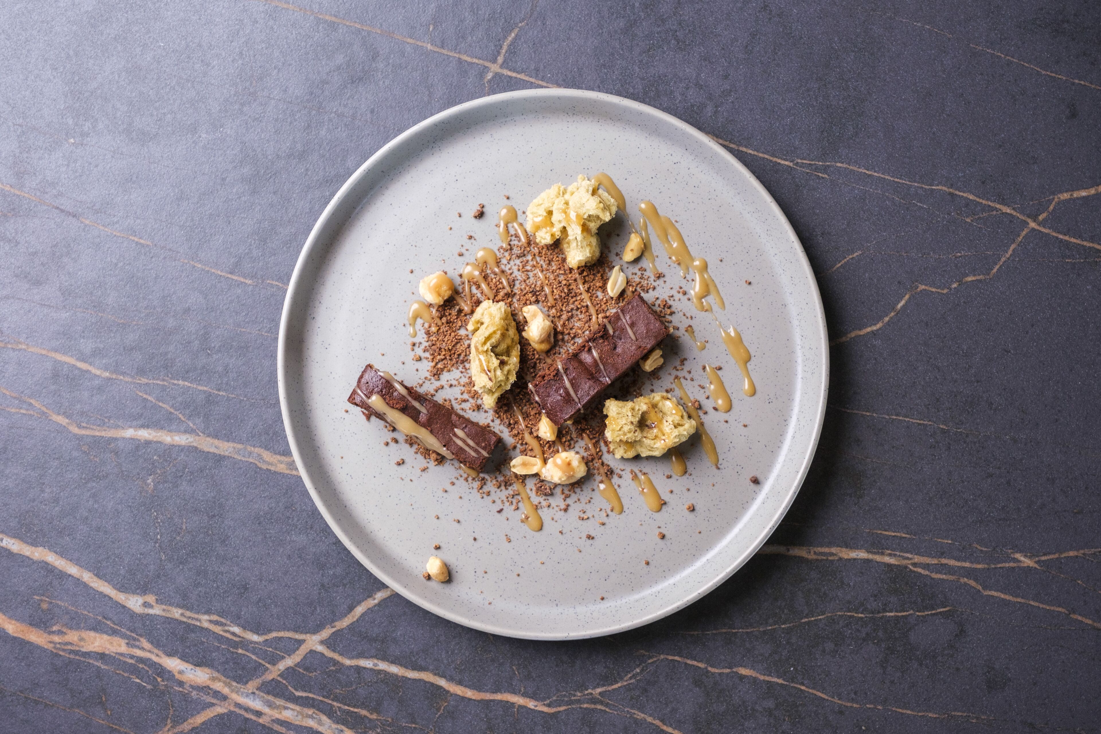 A dessert plate with chocolate pieces, nuts, and caramel sauce on a marble surface.