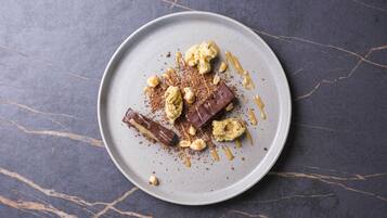 A dessert plate with chocolate pieces, nuts, and caramel sauce on a marble surface.