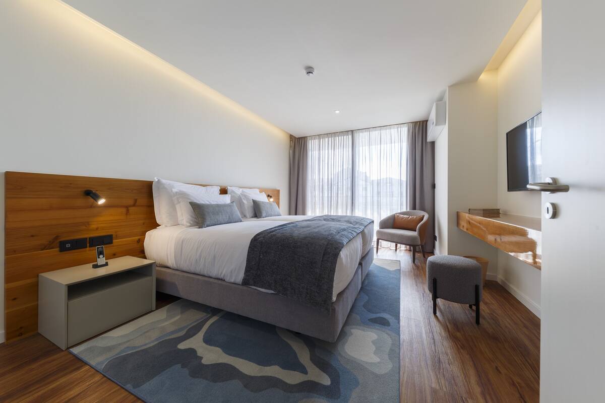 A modern hotel room with a large bed, bedside tables, a seating area, and a TV.