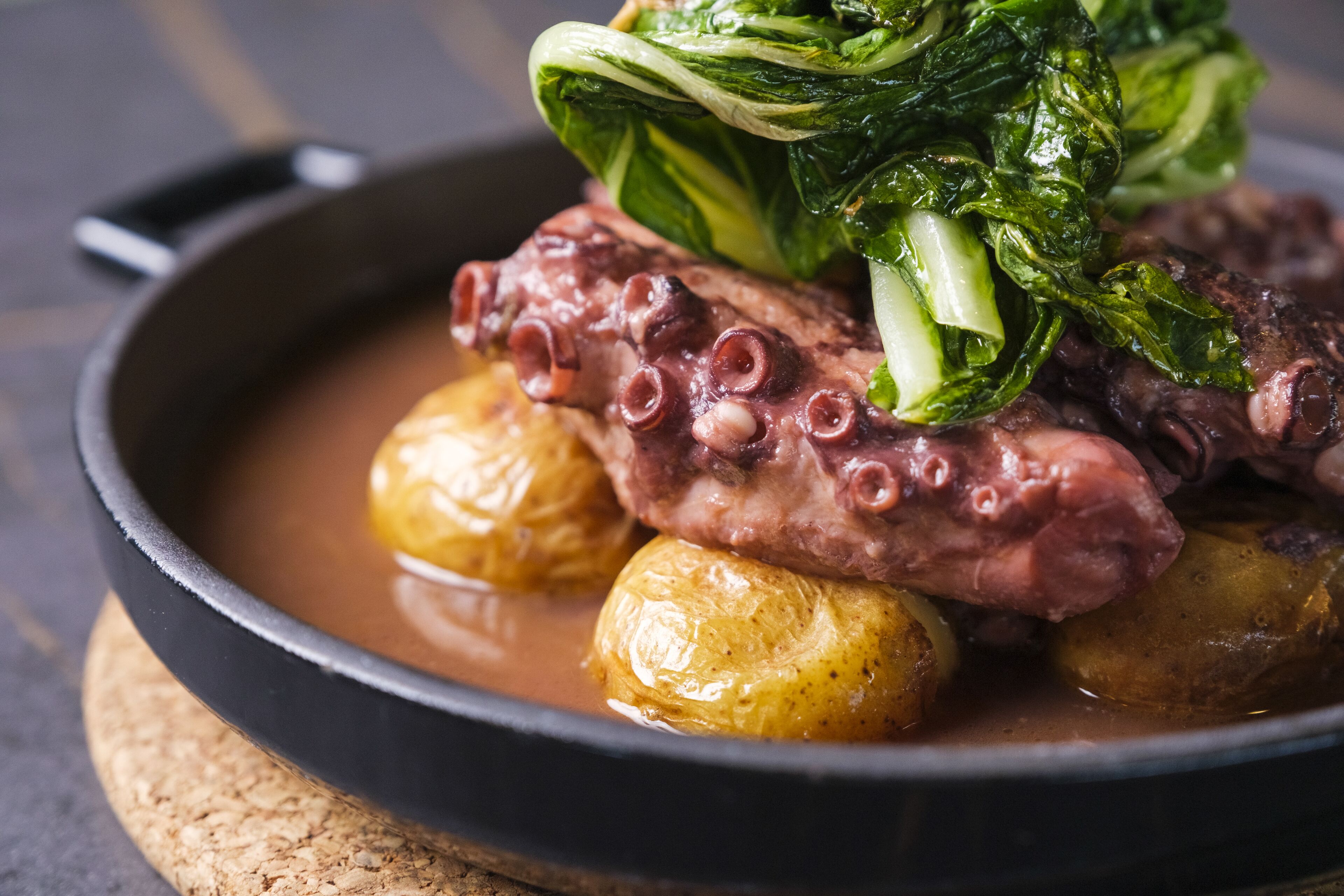 A dish with octopus, potatoes, and greens in a pan.