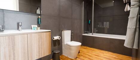 A modern bathroom with a wooden vanity, a toilet, and a glass-enclosed shower.