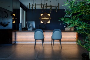 Een receptiezone met een modern ontwerp, met een donkere wand met een geometrisch sign, twee grijze stoelen, een houten receptiebalie en een potplant.