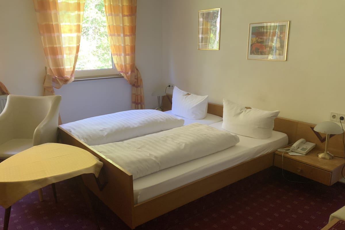 A hotel room with a double bed, a chair, a bedside table with a lamp, and two framed pictures on the wall.