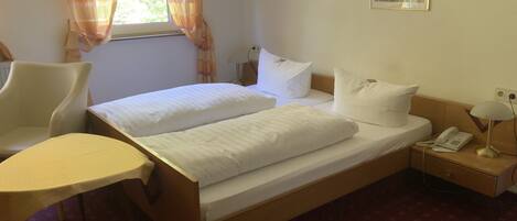A hotel room with a double bed, a chair, a bedside table with a lamp, and two framed pictures on the wall.