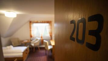 Habitación de hotel con una cama, un escritorio y una silla. La habitación tiene una puerta de madera con el número 203.
