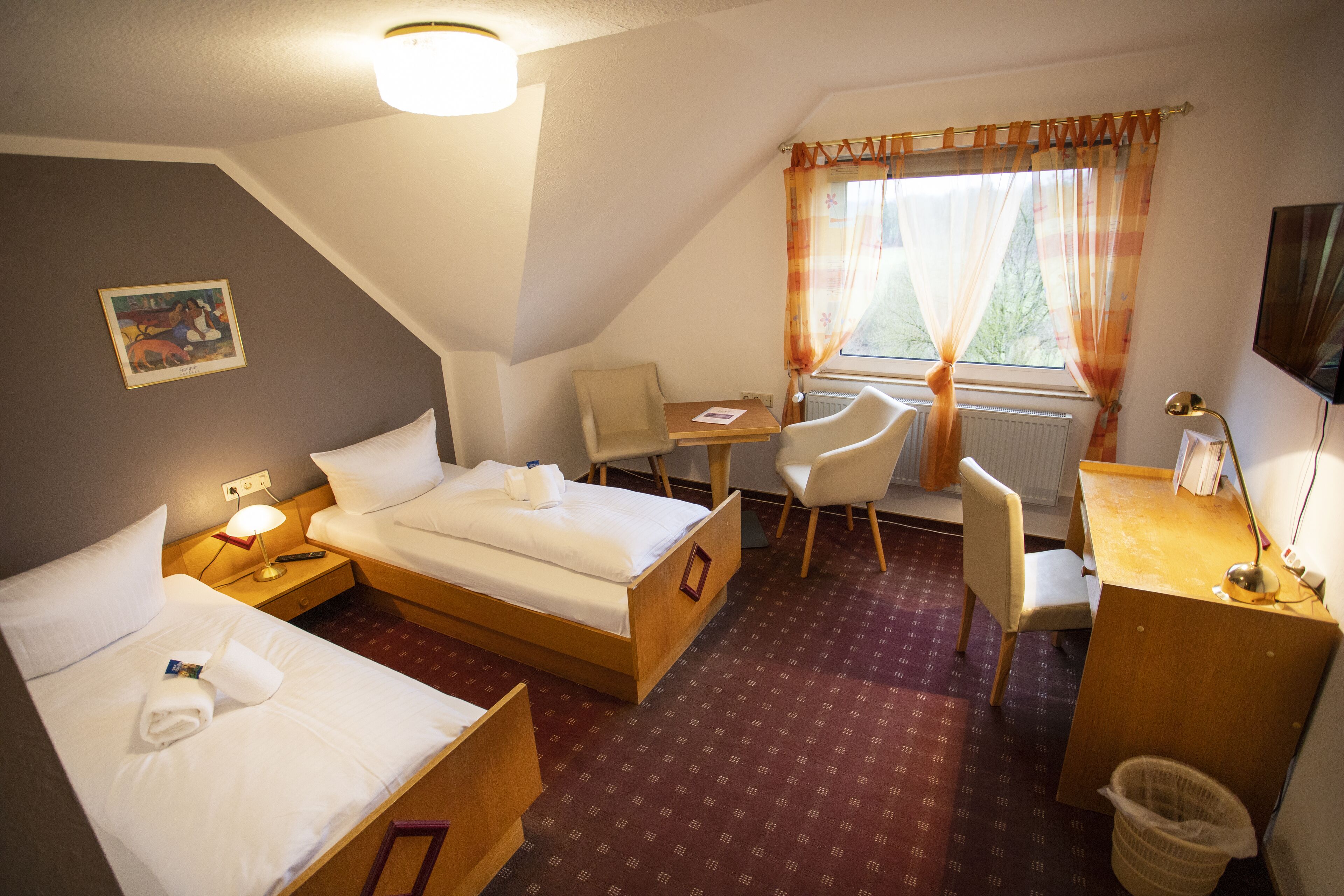 Ein Hotelzimmer mit zwei Betten, einem Schreibtisch, einem Stuhl, einem Fernseher und einem Fenster mit Vorhängen.