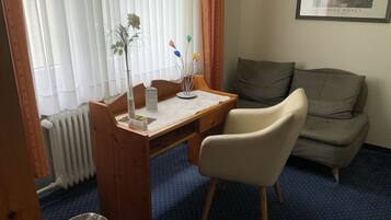 A room with a wooden desk, a chair, a radiator, a framed picture on the wall, and a grey sofa.
