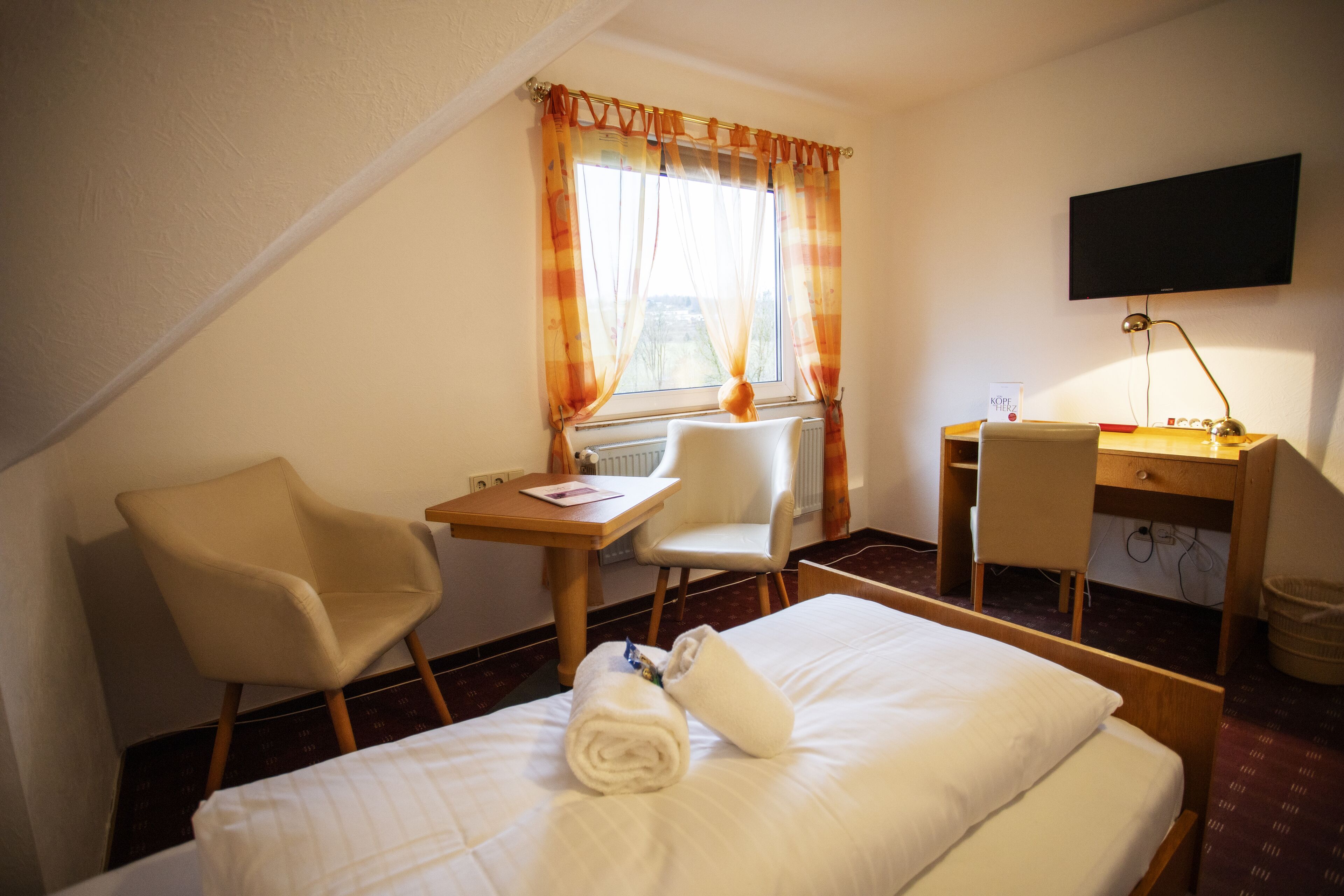 Ein Hotelzimmer mit Bett, Schreibtisch, Stuhl, Fernseher und einem Fenster mit Vorhängen.