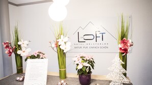Balcão de recepção com logotipo, vasos com flores, uma pequena árvore de Natal e um cartão com informações para hóspedes.