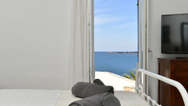 A bed with rolled towels, a television, and a view of the sea. - Kastro Traditional House (Paros)