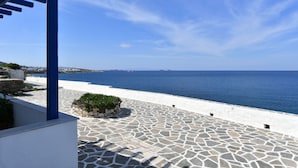 A stone-paved terrace with a view of the sea, a white wall, and a blue structure. - Kastro Traditional House (Paros)