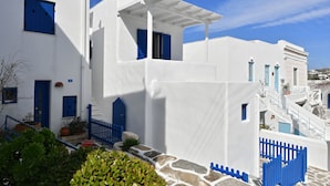 A white building with blue shutters and a stone wall. - Kastro Traditional House (Paros)