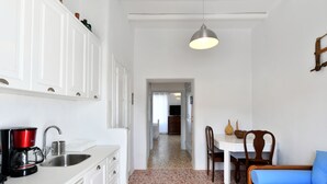 A compact kitchen with a coffee maker, sink, and cabinets. A dining area with a table and chairs is visible in the background. - Kastro Traditional House (Paros)