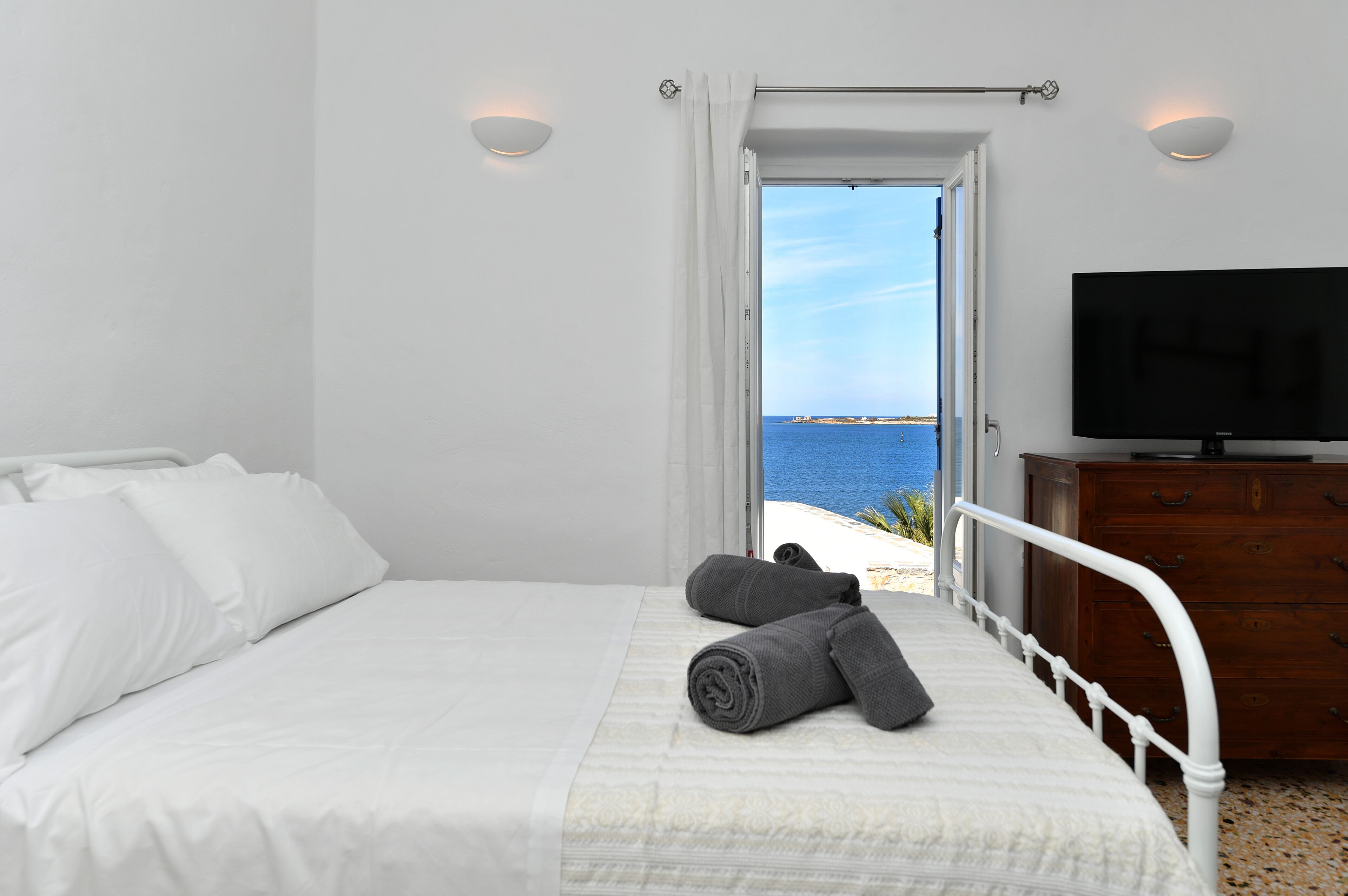 A bedroom with a bed, a TV, and a view of the sea.