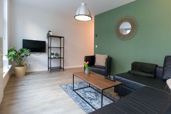 A living room with a TV, sofa, coffee table, and a potted plant.