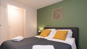 Ein ordentlich bezogenes Bett mit weißen und senffarbenen Kissen, einem dunklen Kopfteil und einem geometrischen Kunstwerk an der Wand.