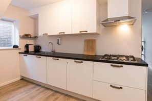 A modern kitchen with white cabinets, a black countertop, a gas stove, and a window with blinds.
