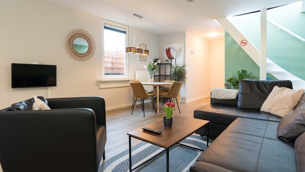 Ein modernes Wohnzimmer mit Sofa, Couchtisch, Fernseher und einem Essbereich mit Stühlen und Tisch.